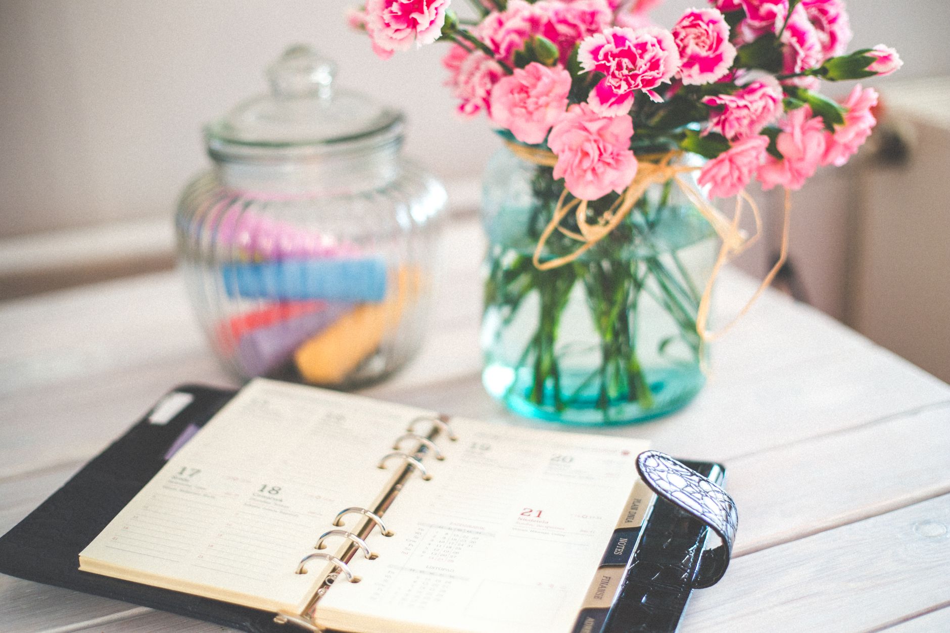 An open planner on a desk beside a vase of flowers